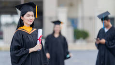 一名身穿毕业礼服的年轻貌美的亚洲女大学毕业生在参加完大学毕业典礼后，持学位证书站在大学大楼前