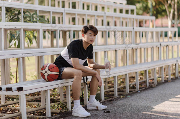 体育与娱乐<strong>的</strong>概念一个<strong>年轻的男性</strong>篮球运动员坐在体育场边界<strong>的</strong>看台上.