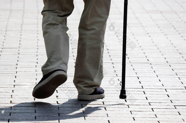 一个拿着手杖走在街上的人。<strong>老年</strong>、脊柱疾病或关节疾病、<strong>老年</strong>人的概念