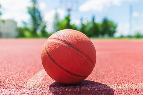 橙色的老篮球运动在篮球场上的红色橡胶球场上。阳光明媚的夏天温暖的天气。模糊的背景。橙色的球在等待着球员。复制空间.