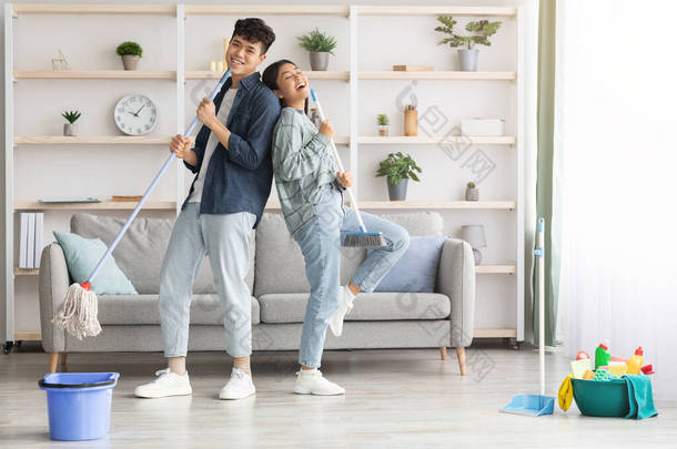 Happy asian couple singing songs while cleaning apartment, copy space