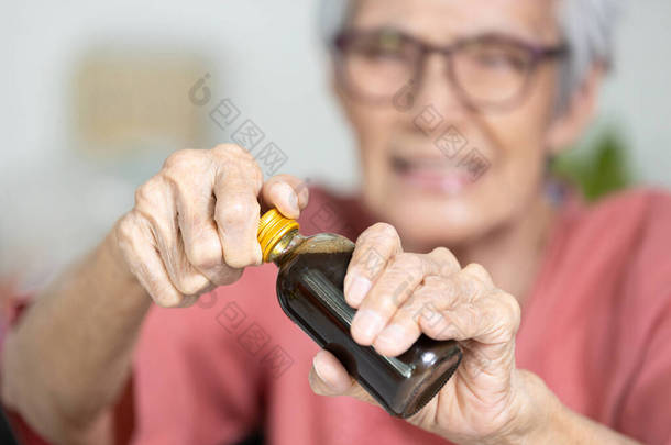 亚洲的老年妇女手里拿着一瓶液体药物，年迈的老人却很难打开瓶盖，打开瓶盖时拧紧瓶盖，难以打开，手指头软弱无力，肌肉无力