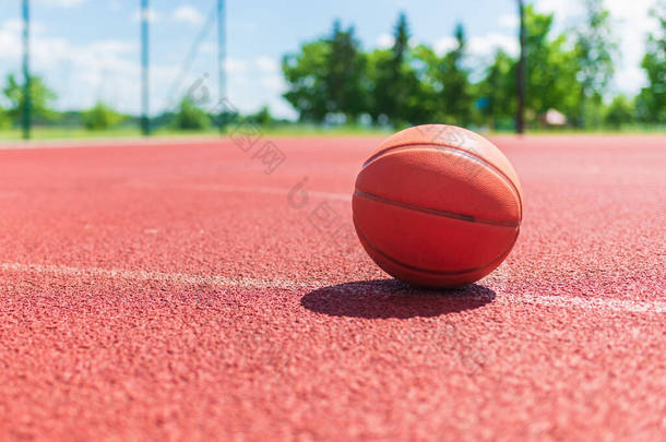 橙色旧篮球场上的红色橡胶球场。阳光灿烂的夏天温暖的天气。模糊的背景。橙色篮球场在等着比赛。复制空间.