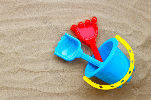 塑料玩具，铲子和桶在白色背景的沙子上。夏季背景概念