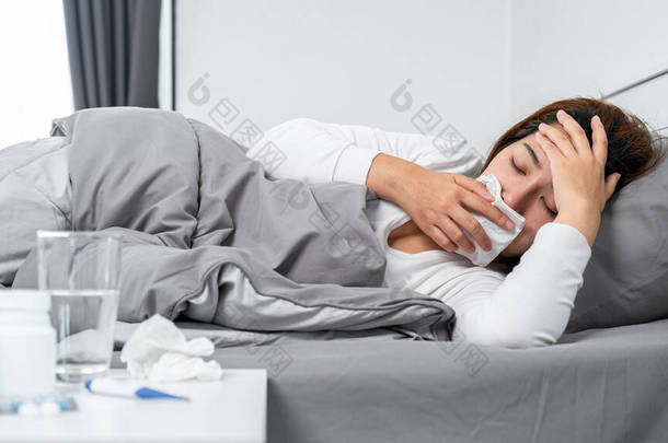 亚洲女人用纸巾捂住你的嘴<strong>咳嗽</strong>、打喷嚏、摸额头时感到不舒服，并用温度计检查体温和吃药后躺在床上