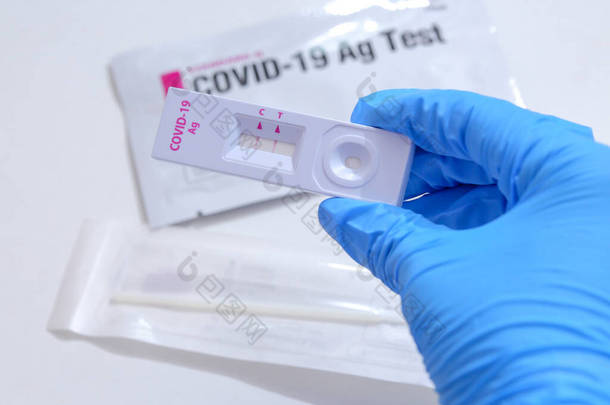 头戴蓝色医用手套、手持COVID-19 (SARS-CoV-2)首个抗原测试仪的女性，可协助在家中进行快速检测。显示COVID-19型流感爆发呈阳性.