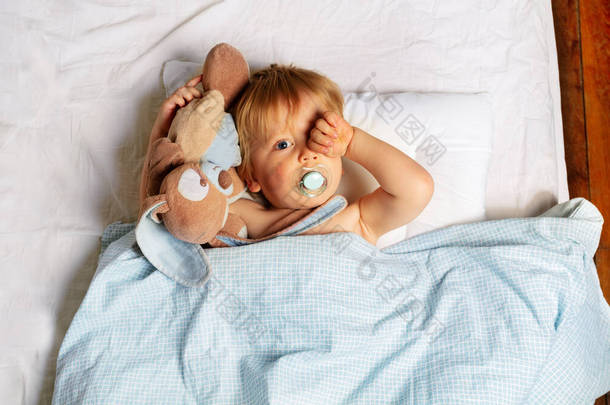 睡梦中的男婴在床上醒来，抱着玩具擦拭着眼睛