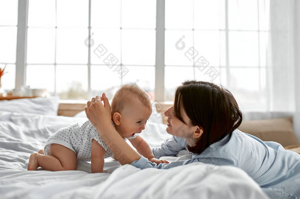 可爱的妈妈在家里抱着新生儿，妈妈和男婴在阳光灿烂的卧室里玩耍。父母和小孩在家里放松。一家人在一起玩得很开心儿童保育、<strong>孕产</strong>概念.