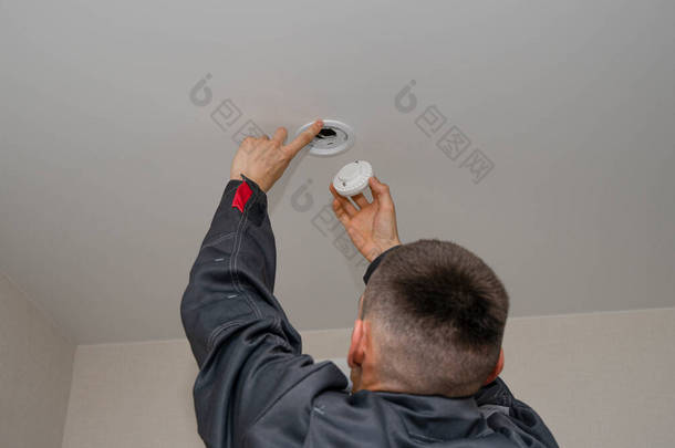 电工在伸展的天花板上安装或更换聚光灯.一位电工在天花板上安装了现代LED灯。节能技术概念。一个电工在工作.