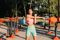在户外运动场地，身强体壮的女子穿着日落时的运动服，在运动结束前伸展肩膀