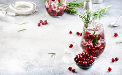 冬季覆盆子混合伏特加、冰块、果汁、迷迭香和红莓。喜庆的长饮。带有负空间的灰色表格背景