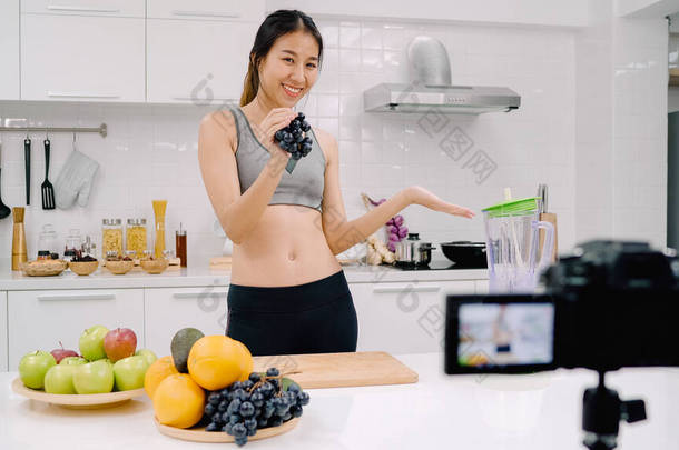 博客运动亚洲妇女使用相机记录<strong>如何</strong>使葡萄汁视频为她的订户, 女性使用有机水果制作葡萄汁自己在家里。健康食品理念.