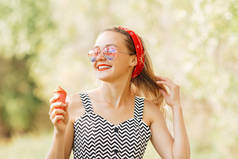 年轻的金发嬉皮士女孩在炎炎夏日戴着太阳镜吃着美味的粉红色冰淇淋，心情很好，面带微笑