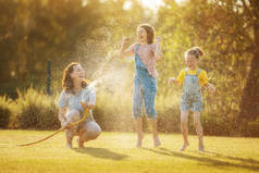 快乐的家庭在后院玩耍。妈妈在炎炎夏日给孩子们浇水.