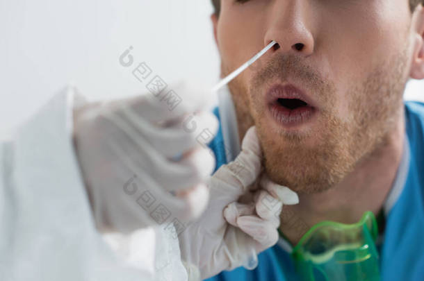 手握乳胶手套的医生在做鼻腔pcr检查时，对卷曲病人近鼻部擦拭进行局部透视