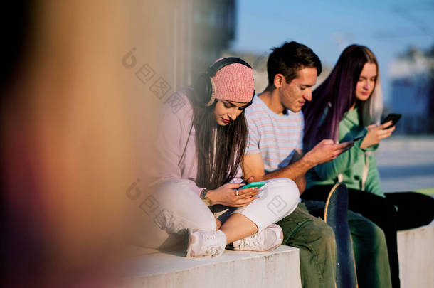 三个十几岁的朋友坐在城市的外面，挂着他们的电话.