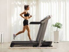 一名健康的年轻女子在家里的跑步机上奔跑时的全长侧面照