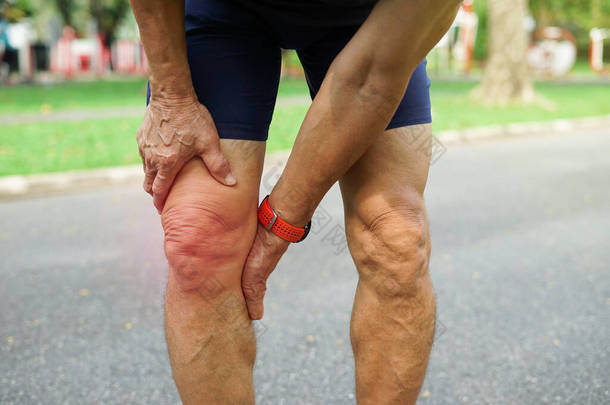 一位老人在公园里锻炼时支撑着他的膝盖，老年人因运动而感到膝盖疼痛.