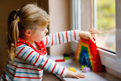 可爱的小女孩通过窗户创造彩虹与五彩斑斓的塑料块大流行病验尸检疫。世界各地的孩子们做的彩虹和画的彩虹都是标志.