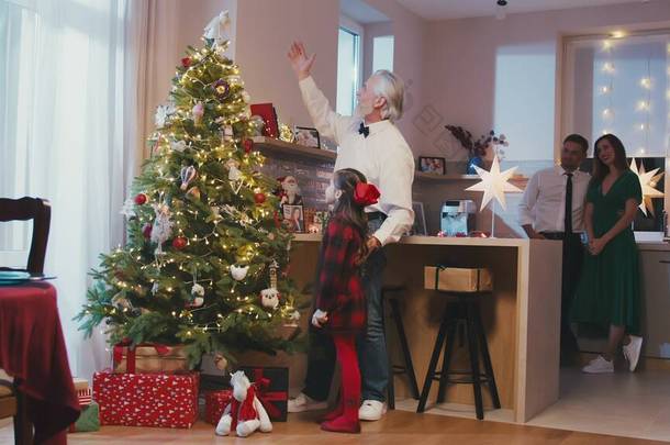 在圣诞节或新年派对上，快乐的祖父和孙女在圣诞树旁挂着装饰品。圣诞节庆祝<strong>准备活动</strong>或寒假.