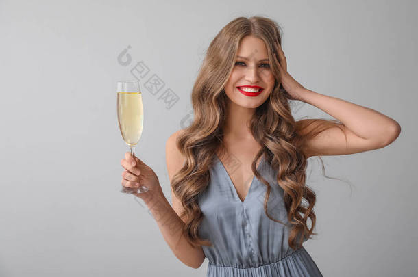 Beautiful young woman with champagne on grey background