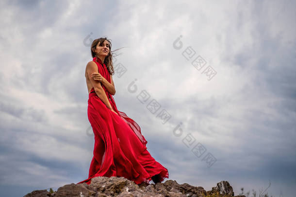 一个穿着红色衣服的女人站在暴风雨的天空之上，裙子<strong>飘扬</strong>，面料在风中<strong>飘扬</strong>.