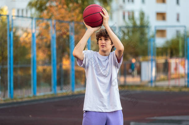 穿着白色T恤的可爱少年在外面<strong>打篮球</strong>。年轻的男孩带着球学习<strong>运球</strong>和射击在城市的球场。孩子的好色，积极的生活方式