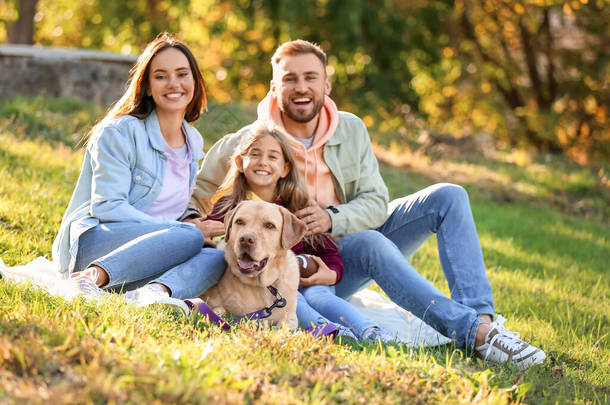 Happy family with Labrador dog sitting on plaid in park