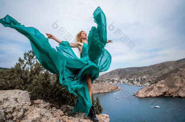 一个穿着翡翠衣服的女人，一个穿着<strong>飘</strong>逸的长丝翅膀的时装模特，在堤岸上<strong>飘</strong>扬着面料.