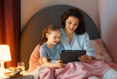 快乐温馨的家庭。年轻的母亲和女儿使用平板电脑。妈妈和可爱的孩子在家里玩得很开心.
