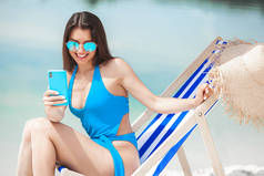 夏天，海滩上拿着手机的女人。女士在讲电话。女性用智能手机拍照.