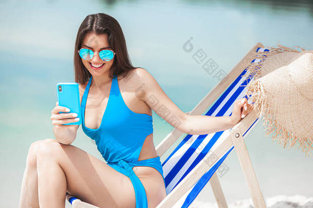 夏天，海滩上拿着手机的女人。女士在讲电话。女性用智能手机拍照.