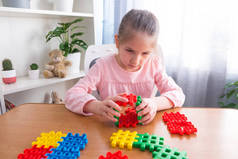 一位6岁至7岁的小女孩穿着粉色T恤，带着一只泰迪熊坐在桌旁，收集拼图.