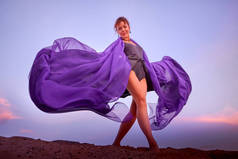 美丽的姑娘,穿着黑色的衣服,紫罗兰飘逸的布,在沙丘上跳舞.模特或舞蹈演员在自然景观中的表演