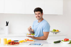 一个英俊的年轻人在午休时间吃着健康的食物，盘子里的蔬菜在厨房里呈浅色。生活方式、健康和营养.