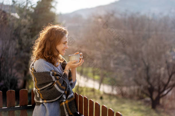 Happy cheerful beautiful curly young woman enjoying morning coffee and mountain view on the terrace 