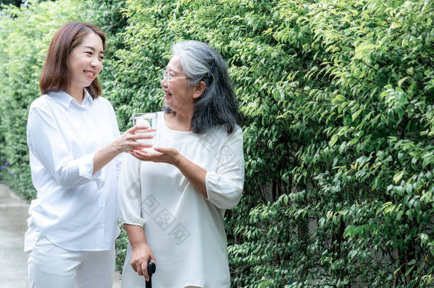 亚洲妇女护理的肖像形象把一杯水递给有绿色背景的老年妇女、护理之家和老年人保健概念.