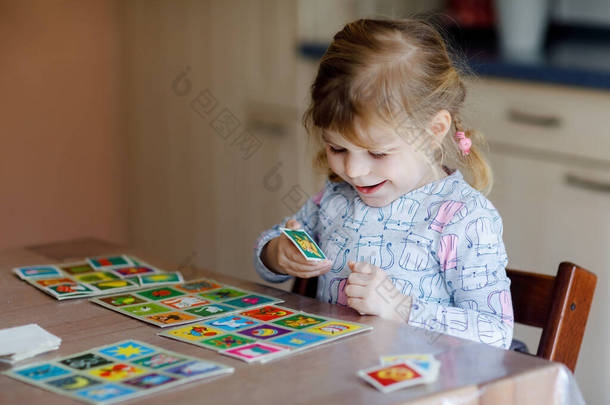 兴奋的笑着可爱的蹒跚学步的小女孩玩着纸牌游戏.快乐健康的孩子训练记忆力，思考。有创意的室内休闲和儿童教育.在家的家庭活动.