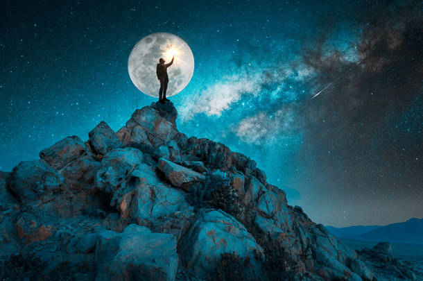 在<strong>星夜</strong>和满月的映衬下，人站在岩石上