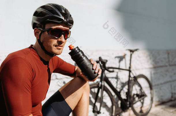在户外运动中，戴着头盔和眼镜的高加索骑自行车者在休息时喝运动瓶子里的水。体育活动后的更新.