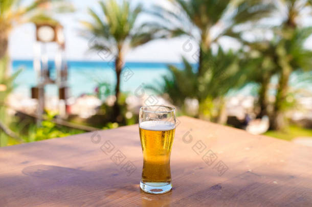大海前木制桌子上的一杯啤酒，蓝蓝的大海和蓝天作为背景
