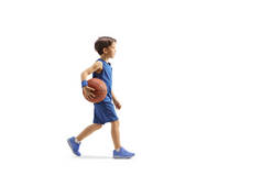 一个穿着蓝色球衣的男孩走路，拿着一个白色背景的篮球，照片全长