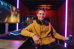 Smiling caucasian pro gamer sitting by gaming setup at home