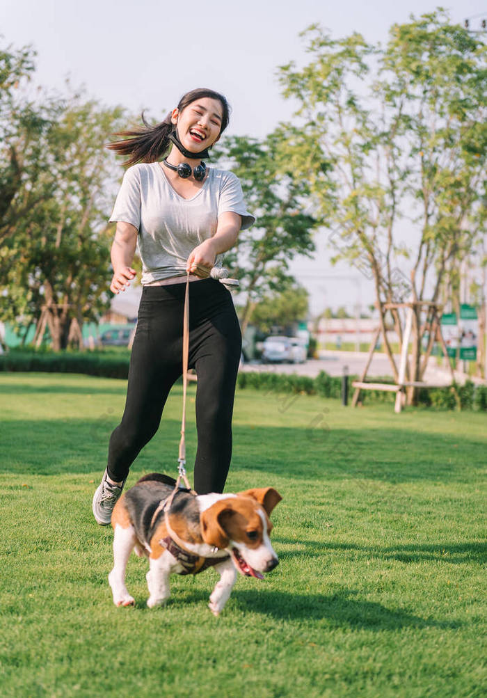 年轻的女运动员和她的小猎犬一起玩耍，带着狗皮带在公园里散步，晚上很开心