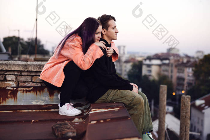 一对年轻夫妇坐在大楼的顶部看着风景拥抱在图片-包图网企业站