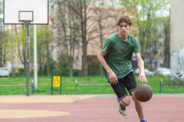 穿着绿色T恤、头戴球衣的可爱少年在球场上打篮球。体育、业余爱好、男孩的积极生活方式
