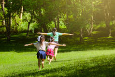 两个可爱的女儿和妈妈一起跑着，张开双臂，好像在春天的花园里一样。后视镜看到年轻的母亲在公园里和孩子们玩耍。快乐的家庭在公园里玩得开心.