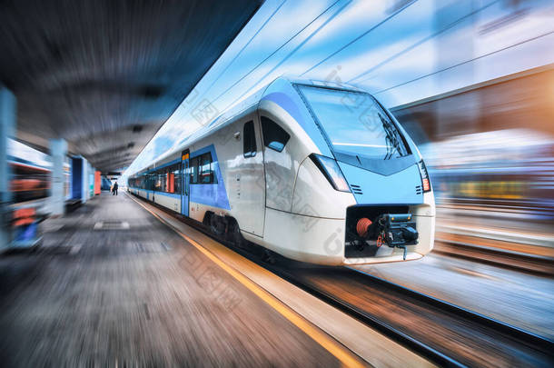 日落时,高速列车在火车站上行驶.蓝色的现代城际客运列车在铁路站台上的运动模糊效果。欧洲的铁路。商业运输