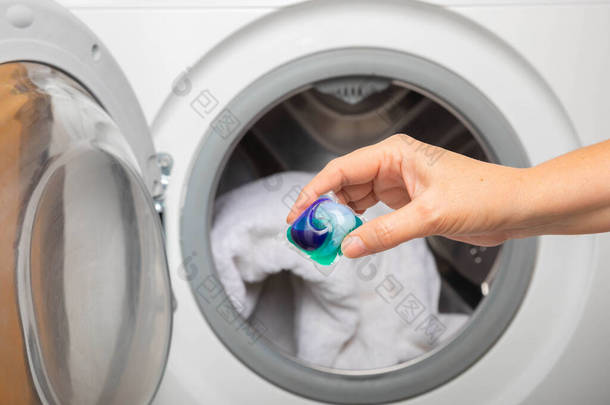女人把洗衣粉胶囊放进洗衣机里，密闭。多彩的洗衣粉生态凝胶在胶囊里。清洗衣物。清洗及洁净的概念