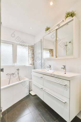 带有镜子和干净浴缸的水槽位于带有玻璃门的淋浴间附近，现代浴室有白色的瓷砖墙图片